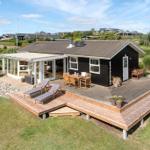 Schwarzes Haus mit Terrasse, Garten und Sonnenschutz. Holztische und Liegestühle.