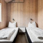 Zwei Einzelbetten mit weißen Bettwäschen und Decken. Holzwände und Fenster. Heizung in der Mitte.