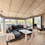 Wohnzimmer mit Sofa, Kamin und großen Fenstern. Holzboden und Holzwände.