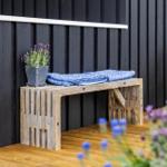 Holzbank mit blauer Decke und Lavendel vor schwarzem Hauswand