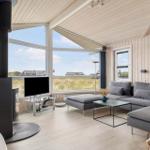 Wohnzimmer mit Holzwänden, großem Fenster und grauem Sofa. Holzdecke und Kaminofen sichtbar.