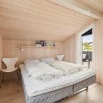 Schlafzimmer mit Holzwand, Bett und Stuhl. Fensterblick auf Terrasse.