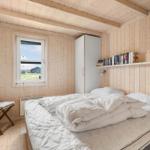Schlafzimmer mit Holzwand, Bett, Stuhl und Bücherregal.