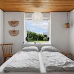Zimmer mit Doppelbett, Fensterblick auf Garten, Holzdecke und Wanddekoration.