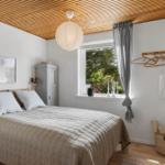 Schlafzimmer mit Bett, Fenster, Holzdecke und Schrank. Wandregal und Lampe sind sichtbar.