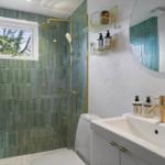 Badezimmer mit grünen Fliesen, Dusche, Waschbecken und Spiegel.
