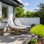 Terrasse mit zwei Liegestühlen, Pflanzen und Blick auf grüne Bäume.