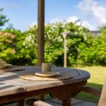Holztisch mit zwei Tassen auf einer Terrasse mit Blick auf grünen Garten.