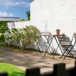 Ein kleiner Gartenbereich mit Tisch und zwei Stühlen an einer weißen Wand.