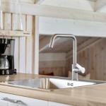 Küchenbereich mit Edelstahl-Spüle und Wasserhahn, Holzoberfläche und Kaffeemaschine.