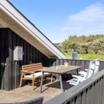 Terrasse mit Tisch, Bänken und Liegestühlen. Hintergrund: Grünflächen und Satellitenschüssel.