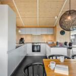 Küche mit Holzwand und -decke, weißer Einbauküche, Esstisch mit Stühlen und Hängelampe.