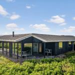 Moderne Villa mit Holzterrasse und großem Glasbereich in grüner Landschaft.