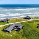 Strandnahe Häuser auf grünem Gelände mit Blick auf das Meer und Wellen.