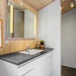 Badezimmer mit Waschtisch, Spiegel und Dusche. Holzwände und weiße Fliesen.
