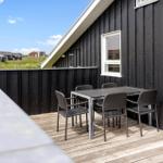 Terrasse mit Tisch und Stühlen an schwarzem Holzhaus mit Blick auf Grasland.
