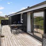 Terrasse mit Tisch, Stühlen und Grill. Blick auf grüne Landschaft. Glasfront zur Wohnung.