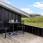Terrasse mit Tisch und zwei Stühlen neben schwarzem Holzhaus mit Blick auf grünes Feld.