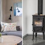 Grauer Sofa mit Stickereikissen, Holztisch und Wandbild. Kaminofen mit brennendem Feuer.