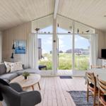 Wohn- und Essbereich mit großem Fenster, Sofa, Tisch und Stühlen. Draußen Grasland und Häuser.