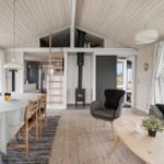 Wohn- und Essbereich mit Holzboden, Esstisch, Sofa und Kaminofen. Helle Fensterfronten mit Blick.