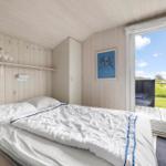 Schlafzimmer mit Bett, Fenster und Holzwand. Draußen ist eine Terrasse mit Blick auf Gras.