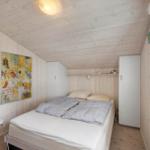 Schlafzimmer mit Bett, weißen Schränken und Holzwand. An der Wand hängt ein Bild.