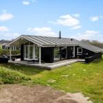 Moderne Holzhütte mit Terrasse und Garten. Blick auf das Haus unter blauem Himmel.