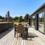 Terrasse mit Tisch, Stühlen und Sonnenschirm. Glasfront führt ins Haus. Blick auf Wald und Himmel.