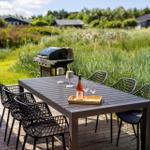 Holzterrasse mit Tisch, Stühlen, Grill und Flasche Wein.