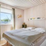 Schlafzimmer mit Holzwandverkleidung, Bett und Fenster mit Vorhängen.