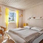 Schlafzimmer mit Holzwand, Bett, Fenster mit gelben Vorhängen und Stuhl.