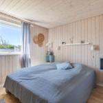 Schlafzimmer mit Holzwand, Bett und Fenster. An der Wand hängen Regale und Dekoration.