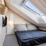 Schlafzimmer mit Dachfenster, Bett und Fernseher an der Wand.