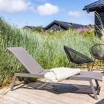 Terrasse mit Liegestuhl, zwei Stühlen und Tisch. Hintergrund: hohe Gräser und dunkle Holzwände.