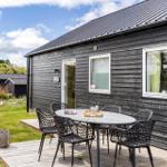 Graues Holzhaus mit Terrasse und Sitzgruppe. Garten und Himmel sind sichtbar.