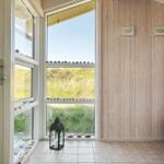 Raum mit Holzwand, großem Fenster und Blick auf Grasland. Bodenfliesen, Laterne und Korb.