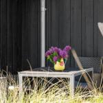Außenbereich mit Tisch, zwei Stühlen und einer Vase mit lila Blumen vor schwarzem Holz.