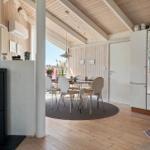 Wohnraum mit Kamin, Esstisch und Küchenbereich unter Holzdecke.