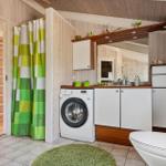 Badezimmer mit Waschmaschine, Spiegelschrank und grünem Duschvorhang.