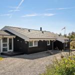 Ein schwarz-weißes Ferienhaus mit Nummer 16, umgeben von Gras und Sträuchern unter blauem Himmel.