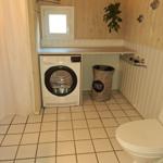 Waschmaschine und Toilette in einem Raum mit Holzwänden und Fliesenboden.