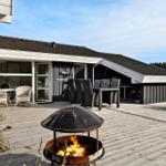 Terrasse mit Grill und Sitzgelegenheiten vor einem Haus mit großem Fenster.