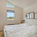 Schlafzimmer mit weißer Bettwäsche, Holzwänden und Fensterblick auf Grünfläche.