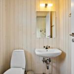 Badezimmer mit Toilette, Waschbecken und Spiegel an Holzwand