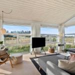 Wohnzimmer mit großem Fenster, Sofa, Fernseher und Holzboden. Blick auf Grasland.