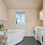 Badezimmer mit Badewanne, Waschmaschine und Fenster mit Blick auf Baum.