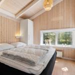 Schlafzimmer mit Holzwand, Bett und Fenster mit Blick auf Bäume.