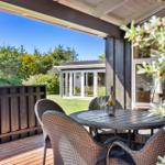 Terrasse mit Tisch und Stühlen, Blick auf grünen Garten und Haus.