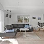 Wohnzimmer mit grauem Sofa, runden Tisch und Holzboden. Durchgang zur Schlafzimmer.